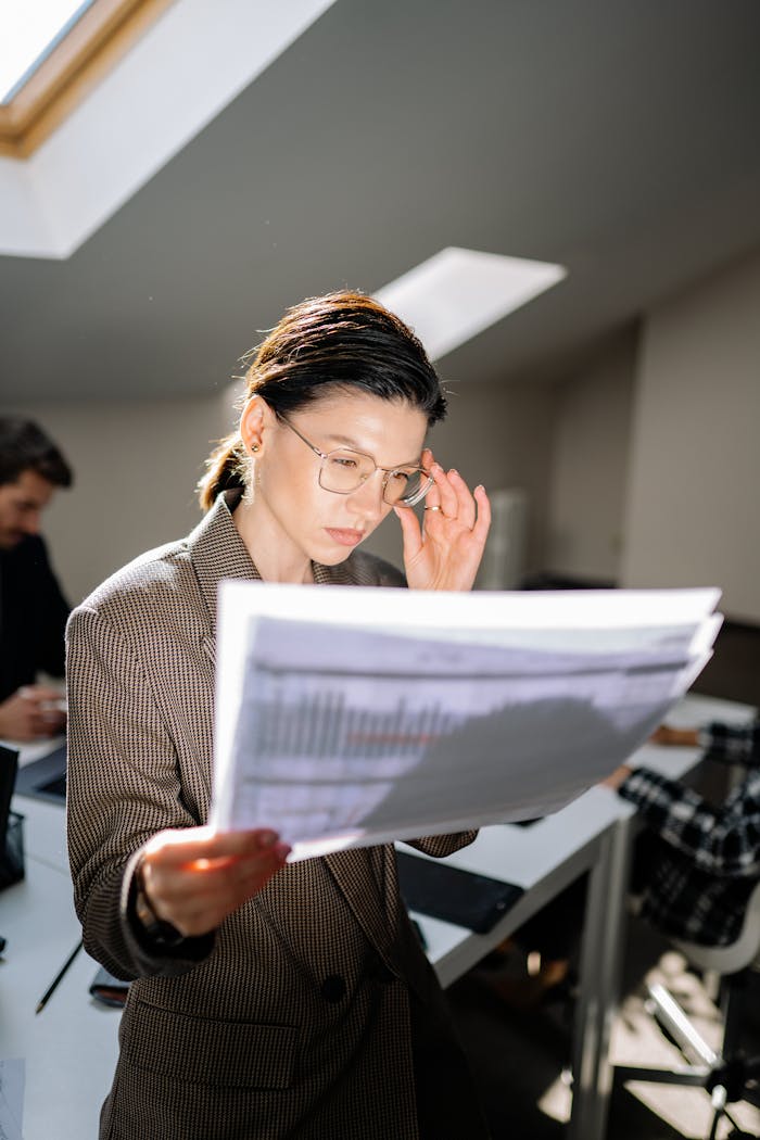 Caucasian woman in office reviewing financial papers under sunlight.